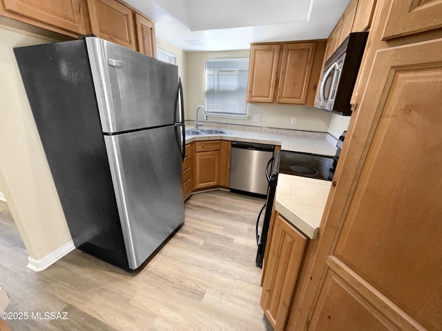 kitchen with appliances with stainless steel finishes, a raised ceiling, sink, and light wood-type flooring