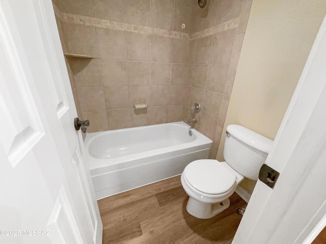 bathroom with hardwood / wood-style flooring, tiled shower / bath, and toilet