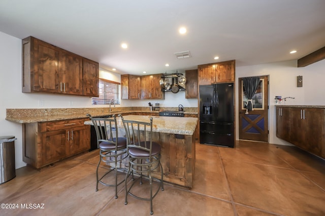 kitchen with a kitchen island, black refrigerator with ice dispenser, sink, and light stone countertops