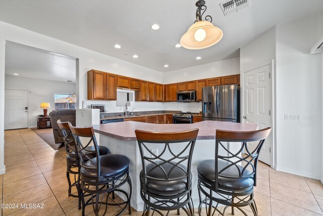 kitchen featuring light tile patterned floors, stainless steel appliances, hanging light fixtures, and a breakfast bar area