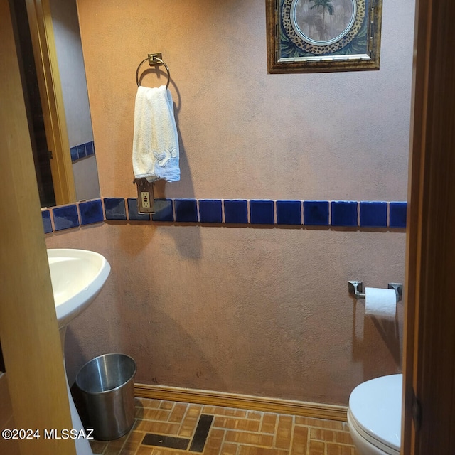 bathroom with brick floor, a sink, and toilet