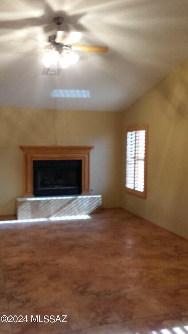 unfurnished living room with a fireplace with raised hearth, lofted ceiling, and a ceiling fan