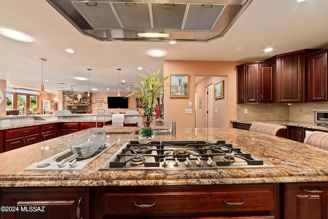 kitchen with light stone countertops, decorative light fixtures, a large island with sink, and stainless steel gas stovetop