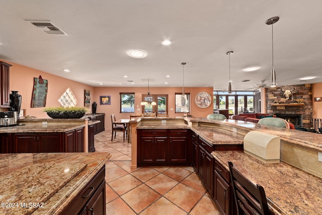 kitchen with pendant lighting, a fireplace, light tile patterned floors, and light stone counters