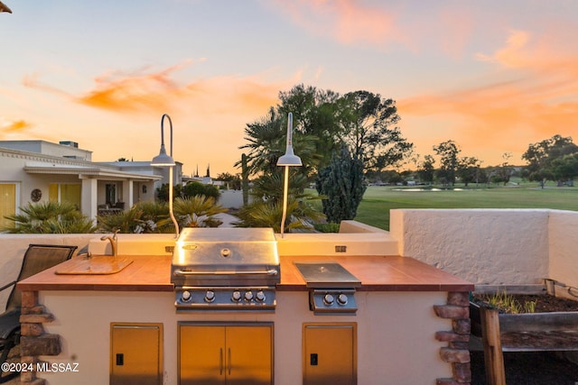 patio terrace at dusk featuring an outdoor kitchen, a yard, and grilling area