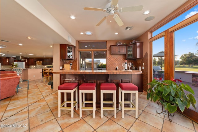 kitchen featuring a kitchen bar, light tile patterned floors, tasteful backsplash, ceiling fan, and white fridge