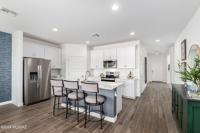 kitchen featuring appliances with stainless steel finishes, a kitchen bar, a kitchen island with sink, white cabinets, and dark hardwood / wood-style flooring