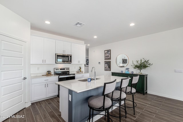 kitchen with stainless steel appliances, white cabinetry, sink, a kitchen island with sink, and dark wood-type flooring