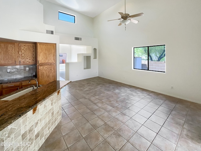 unfurnished living room with ceiling fan, sink, light tile patterned floors, and high vaulted ceiling