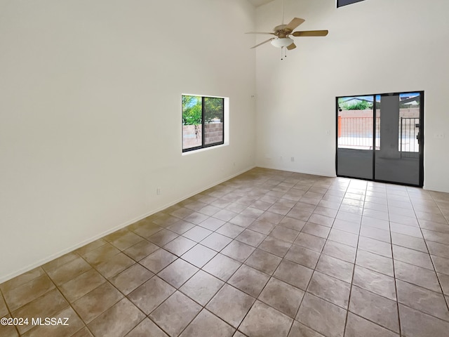 tiled empty room featuring ceiling fan and a towering ceiling