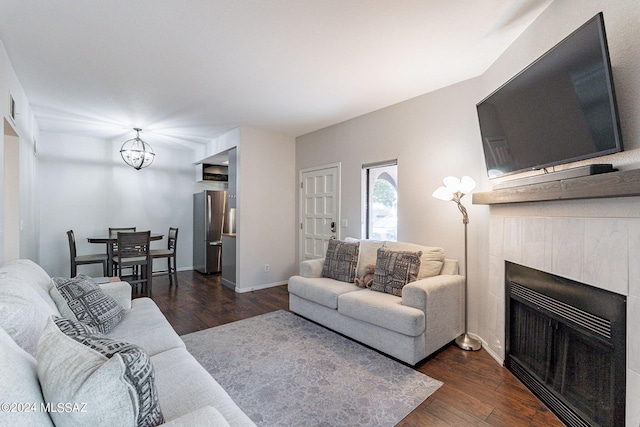 living room featuring a tile fireplace, dark wood-type flooring, and a chandelier