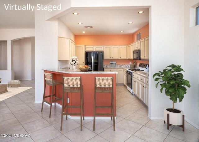 kitchen featuring black appliances, light tile patterned flooring, a kitchen bar, and cream cabinetry