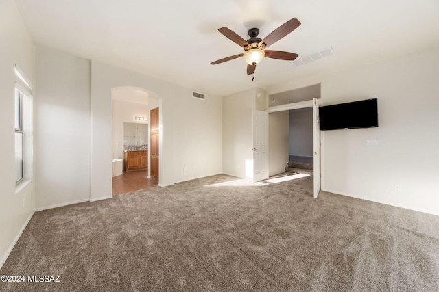 unfurnished bedroom with ensuite bath, carpet, and ceiling fan