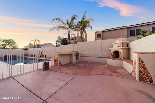 patio terrace at dusk with an outdoor fireplace and a fenced in pool