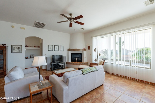 living room featuring a fireplace, light tile flooring, and ceiling fan