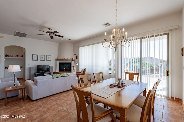 tiled dining area with a fireplace and ceiling fan with notable chandelier