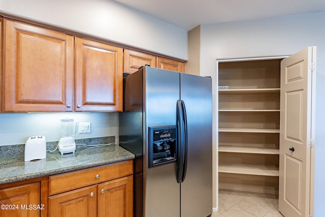 kitchen featuring stainless steel fridge with ice dispenser, dark stone countertops, and light tile flooring