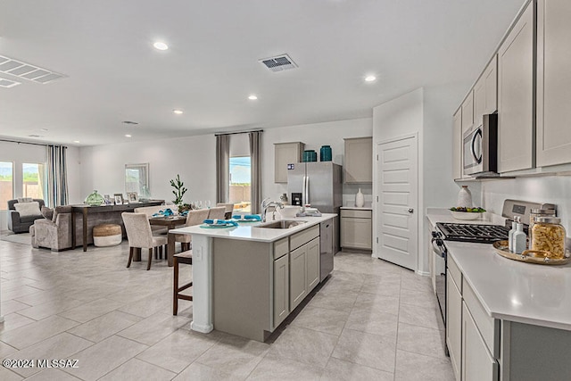 kitchen with sink, an island with sink, gray cabinetry, and stainless steel appliances