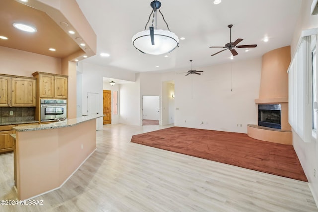 kitchen featuring stainless steel oven, a fireplace, light stone countertops, light hardwood / wood-style floors, and backsplash