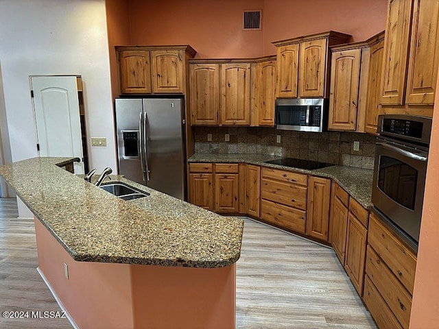 kitchen with appliances with stainless steel finishes, sink, dark stone countertops, backsplash, and a kitchen island with sink