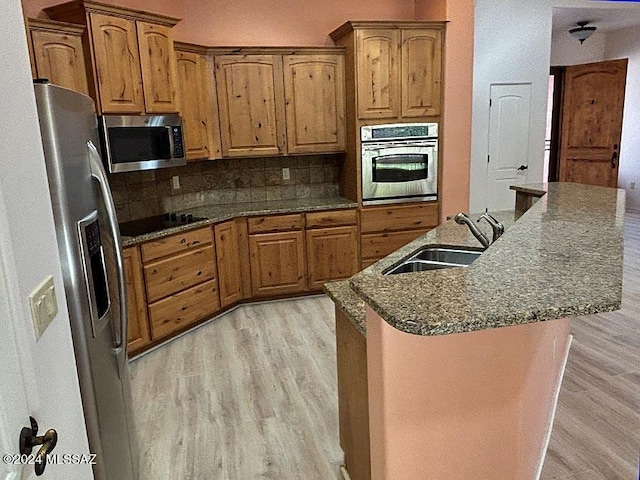 kitchen with sink, a center island with sink, appliances with stainless steel finishes, light hardwood / wood-style floors, and decorative backsplash