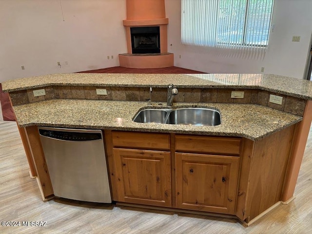 kitchen with dishwasher, sink, light stone countertops, and light wood-type flooring