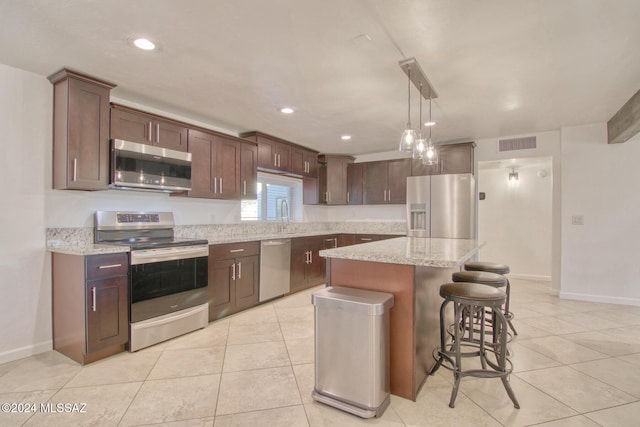 kitchen with a center island, hanging light fixtures, light tile patterned floors, appliances with stainless steel finishes, and light stone counters