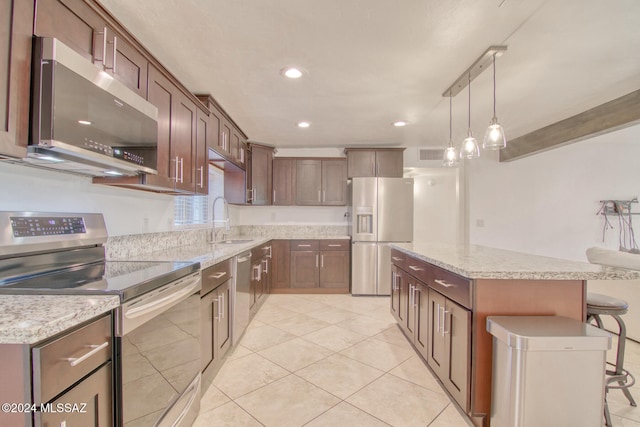 kitchen featuring sink, hanging light fixtures, a kitchen bar, a kitchen island, and appliances with stainless steel finishes