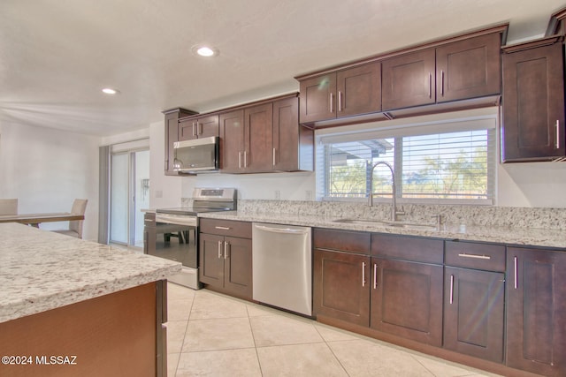 kitchen with sink, light stone countertops, light tile patterned floors, dark brown cabinetry, and stainless steel appliances