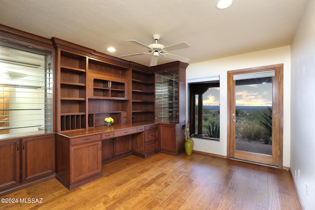 unfurnished office featuring ceiling fan, built in desk, and light wood-type flooring