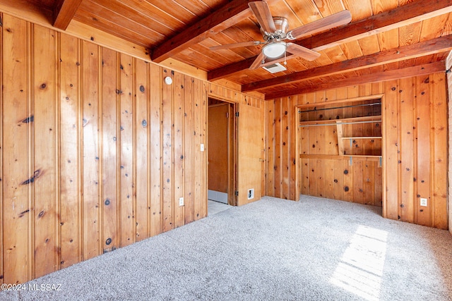 carpeted spare room featuring wooden ceiling, ceiling fan, beam ceiling, and wood walls