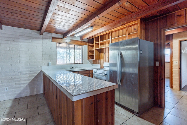 kitchen with brick wall, light tile flooring, white gas range oven, stainless steel fridge, and beam ceiling