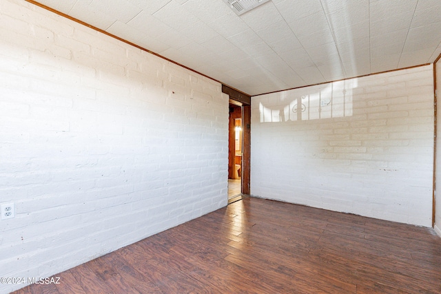 spare room featuring brick wall, dark hardwood / wood-style flooring, and ornamental molding