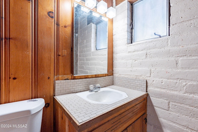 bathroom featuring oversized vanity, toilet, and brick wall