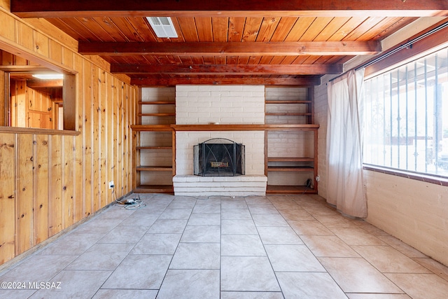 unfurnished living room with wooden walls, beam ceiling, and light tile floors