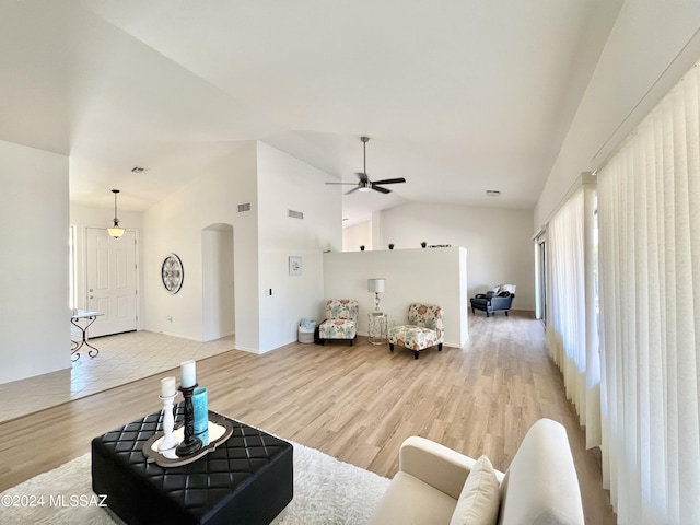 living room with lofted ceiling, visible vents, arched walkways, and light wood finished floors