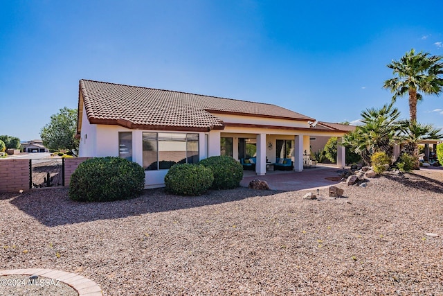 rear view of property with a gate, fence, stucco siding, a tiled roof, and a patio area