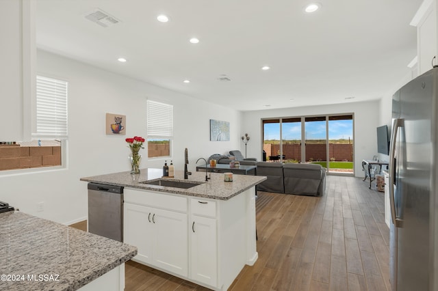 kitchen featuring sink, appliances with stainless steel finishes, light stone countertops, a kitchen island with sink, and white cabinetry