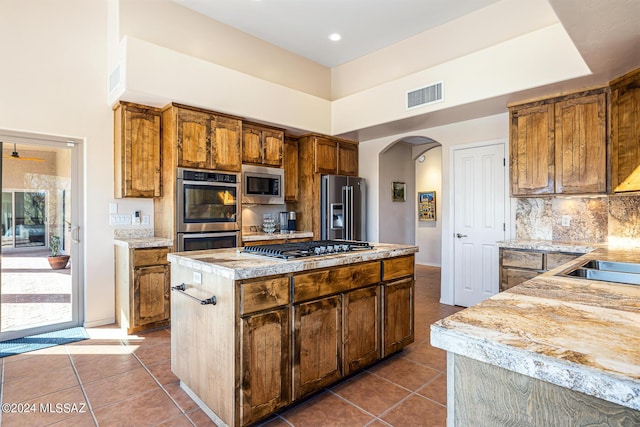 kitchen featuring a towering ceiling, backsplash, stainless steel appliances, dark tile patterned floors, and a center island