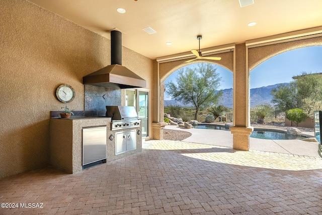 view of patio featuring a grill, a mountain view, ceiling fan, and exterior kitchen