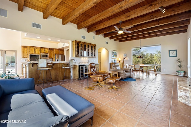 living room featuring tile patterned floors, beverage cooler, ceiling fan, wooden ceiling, and beamed ceiling