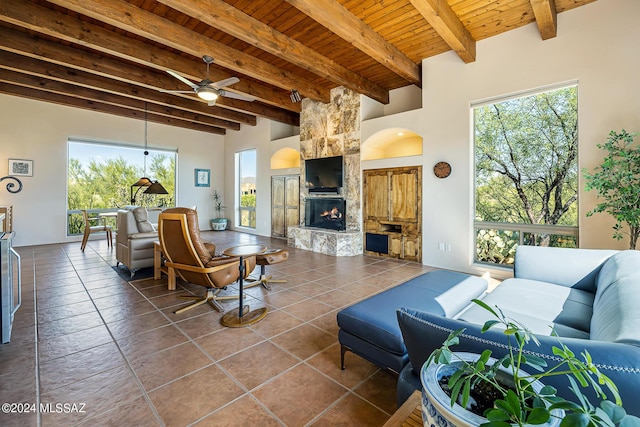 living room featuring wood ceiling, ceiling fan, beamed ceiling, tile patterned flooring, and a stone fireplace