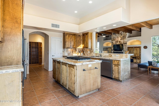 kitchen featuring decorative backsplash, beam ceiling, appliances with stainless steel finishes, a kitchen island, and kitchen peninsula