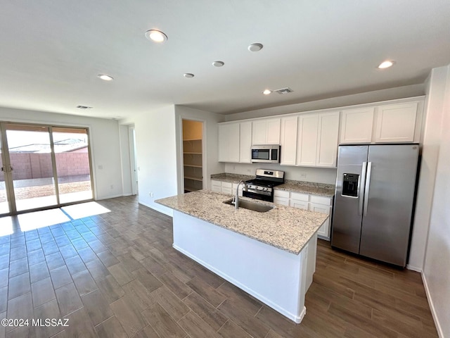 kitchen with a kitchen island with sink, dark hardwood / wood-style floors, light stone countertops, white cabinetry, and stainless steel appliances