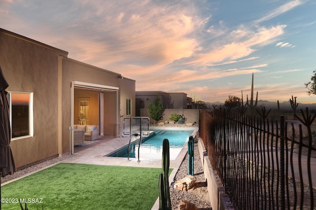 pool at dusk featuring outdoor lounge area, a lawn, and a patio