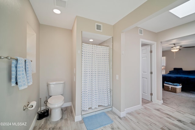 bathroom with a shower with curtain, a skylight, hardwood / wood-style flooring, ceiling fan, and toilet