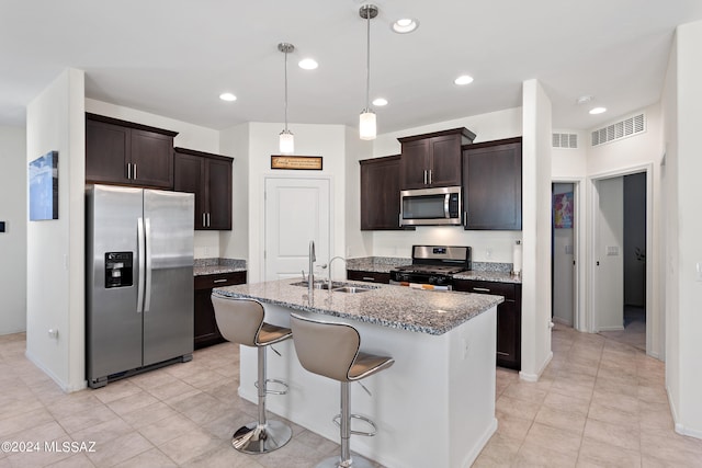 kitchen with a center island with sink, pendant lighting, light tile floors, stone countertops, and appliances with stainless steel finishes