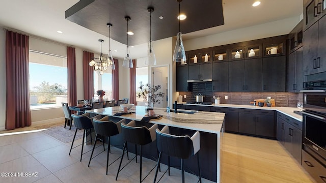 kitchen with an inviting chandelier, a kitchen breakfast bar, an island with sink, pendant lighting, and light tile patterned floors