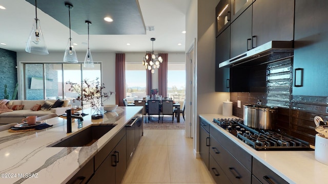 kitchen featuring tasteful backsplash, light stone counters, sink, a chandelier, and hanging light fixtures