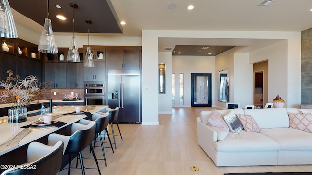 kitchen featuring a kitchen breakfast bar, hanging light fixtures, light stone countertops, appliances with stainless steel finishes, and dark brown cabinets